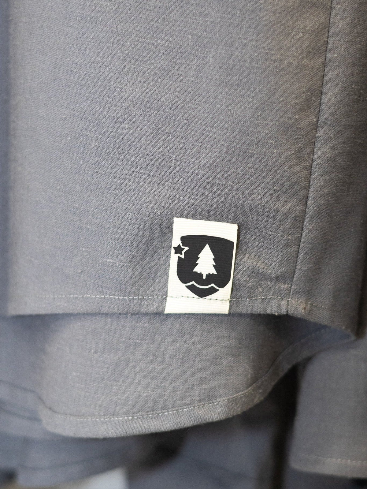 Close-up of a gray heathered fabric garment with a small white rectangular patch featuring a black tree and star logo.